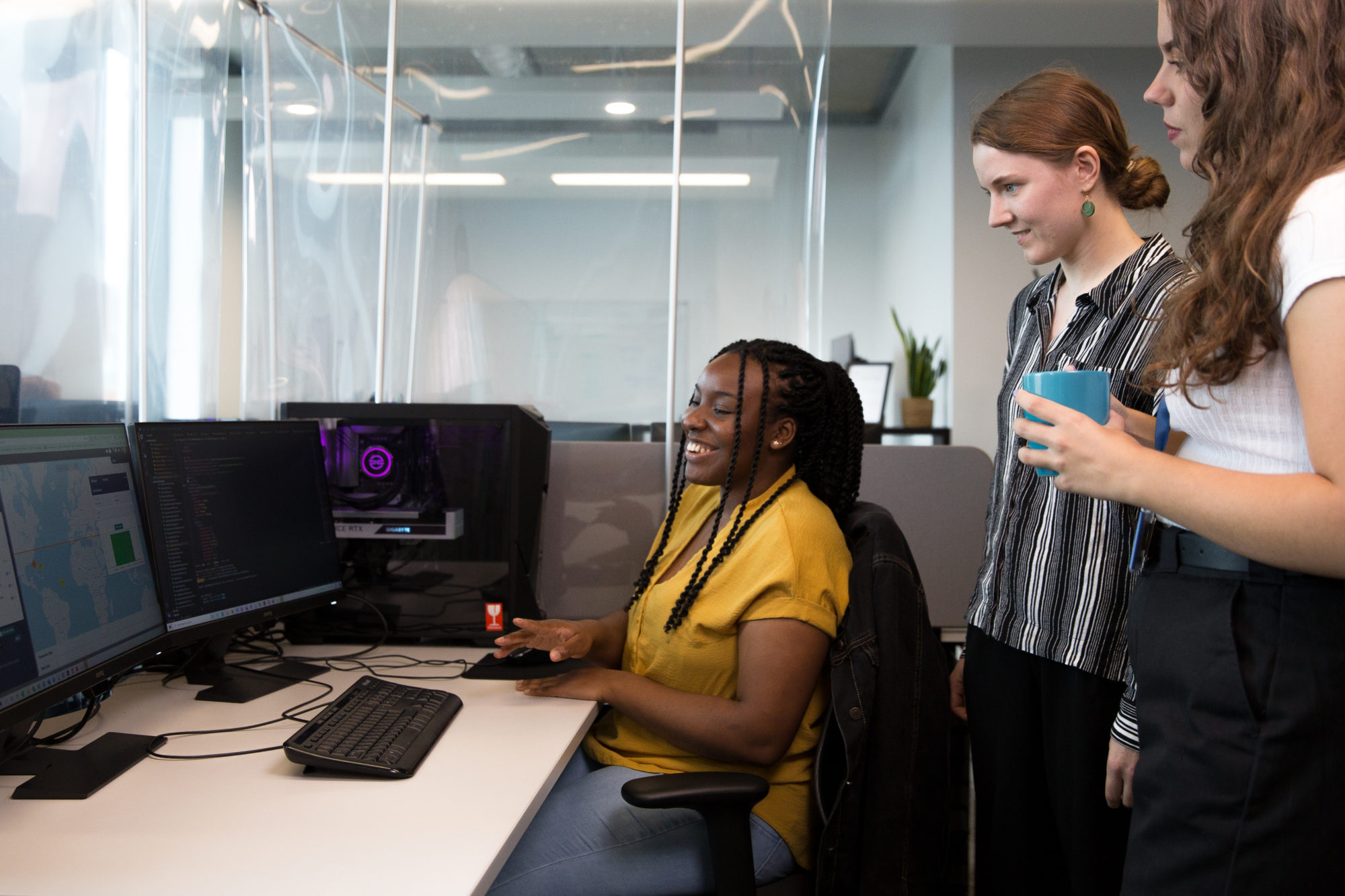 Three female coders from a digital twin company working together around a computer.