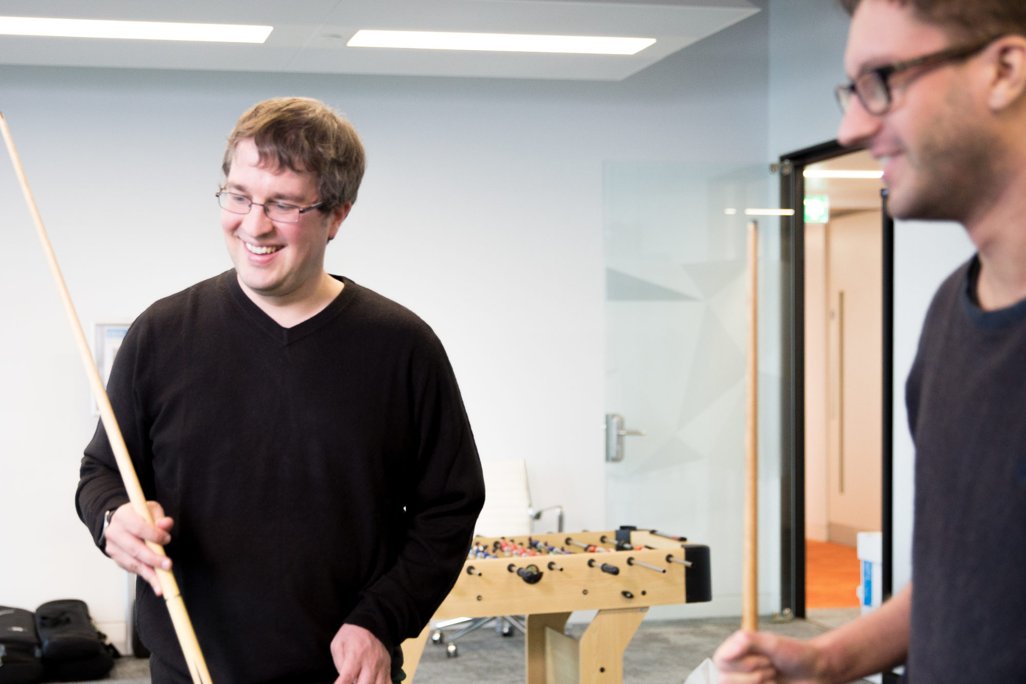 Two employees of Slingshot Simulations laughing and playing pool in the office.