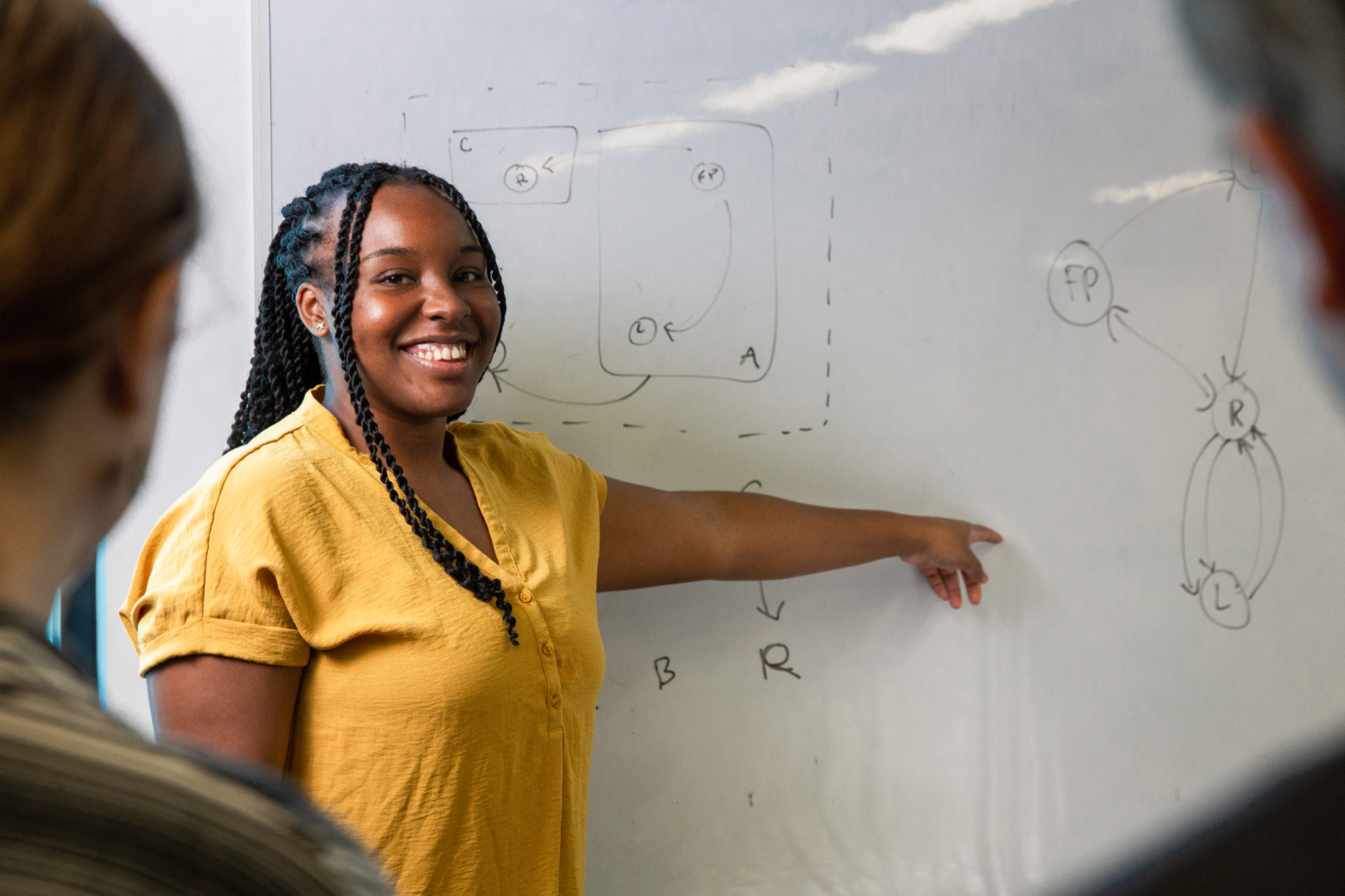 A female employee of Slingshot Simulations pointing at an equation on a whiteboard and smiling widely.