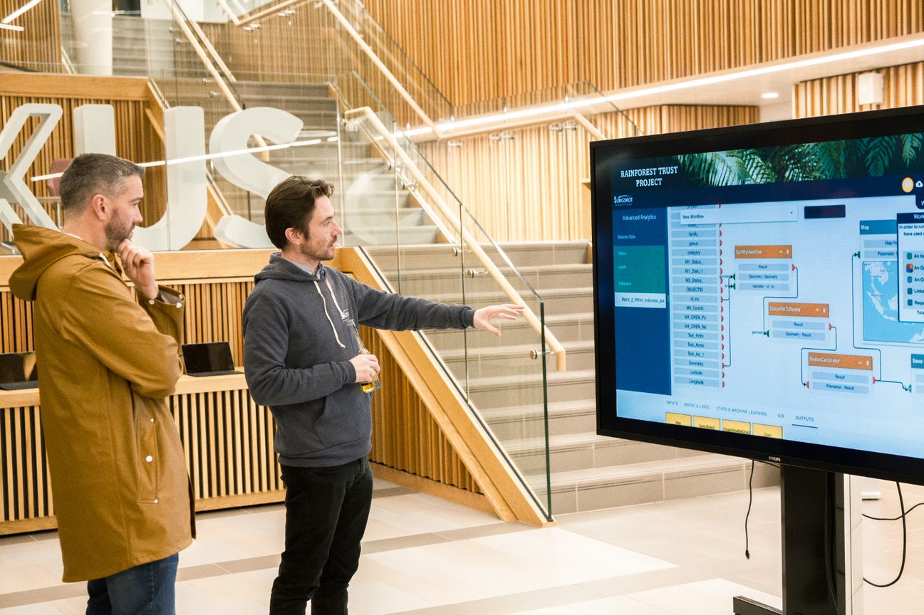 Two Slingshot Simulations employees discussing a software analysis on a large computer screen.